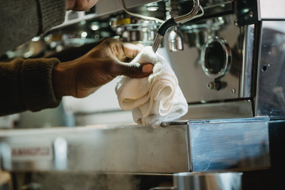 A professional cleaner dressed in a white hazmat suit, mask, and gloves is conducting deep cleaning in a living room using a steam cleaning device that emits visible steam onto a beige carpet. The roo